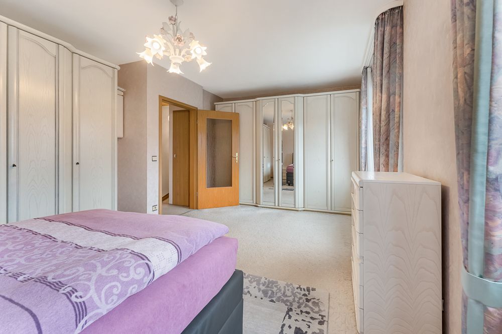Helles Schlafzimmer mit großem Kleiderschrank, Bett, Kommode und offenem Holztürrahmen.