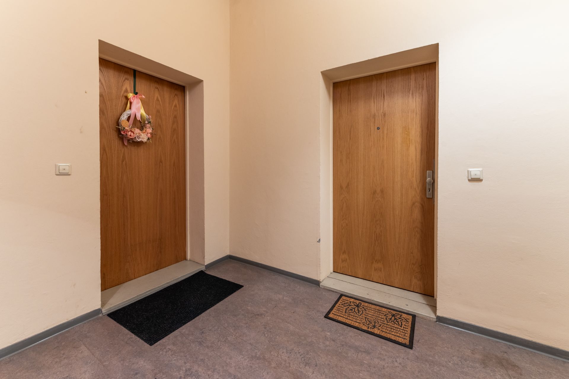 Zwei Wohnungstüren in einem Flur, eine Tür mit Kranz und Teppich, die andere mit Fußmatte.