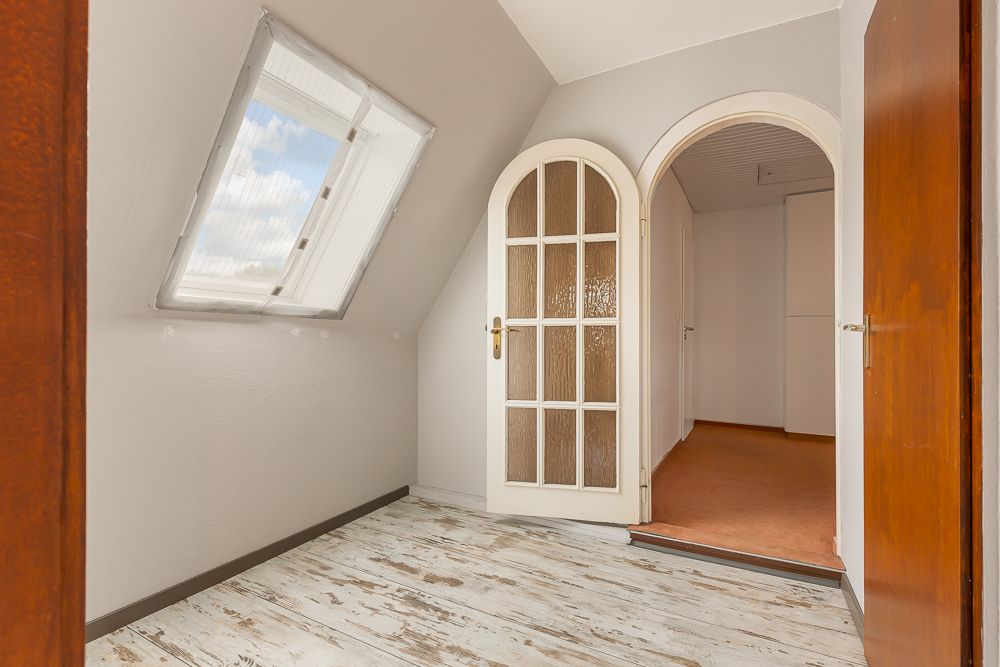 Heller Flur mit großem Fenster, Holztür und Bogen-Türrahmen zu weiterem Raum.