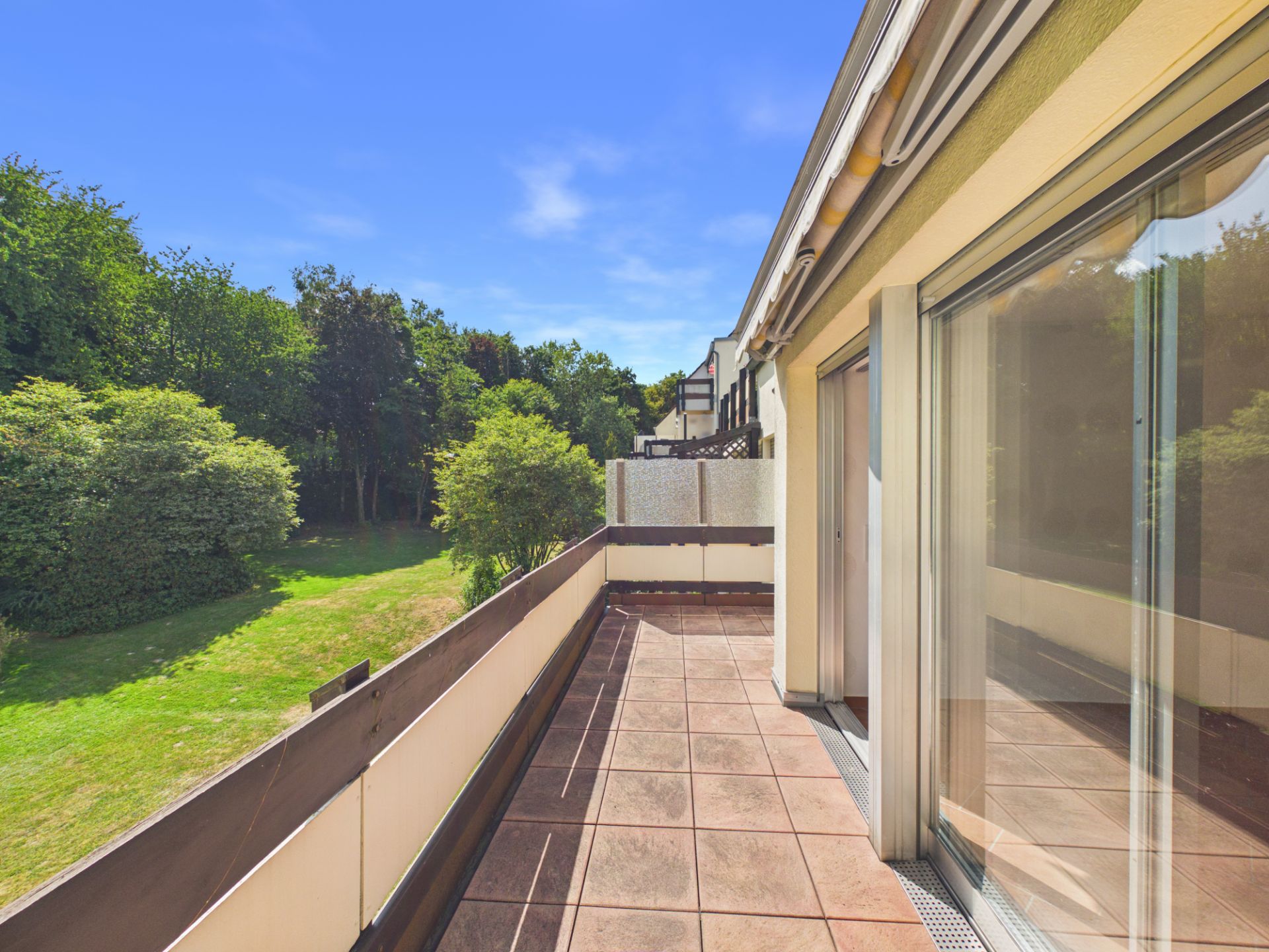 Geräumiger Balkon mit Fliesenboden und Blick auf einen grünen Garten mit Bäumen.