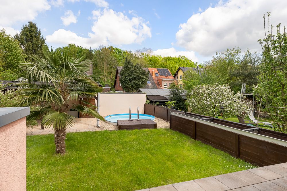 Garten mit Rasen, Palme, kleinem Pool und Holzverkleidung im Hintergrund.