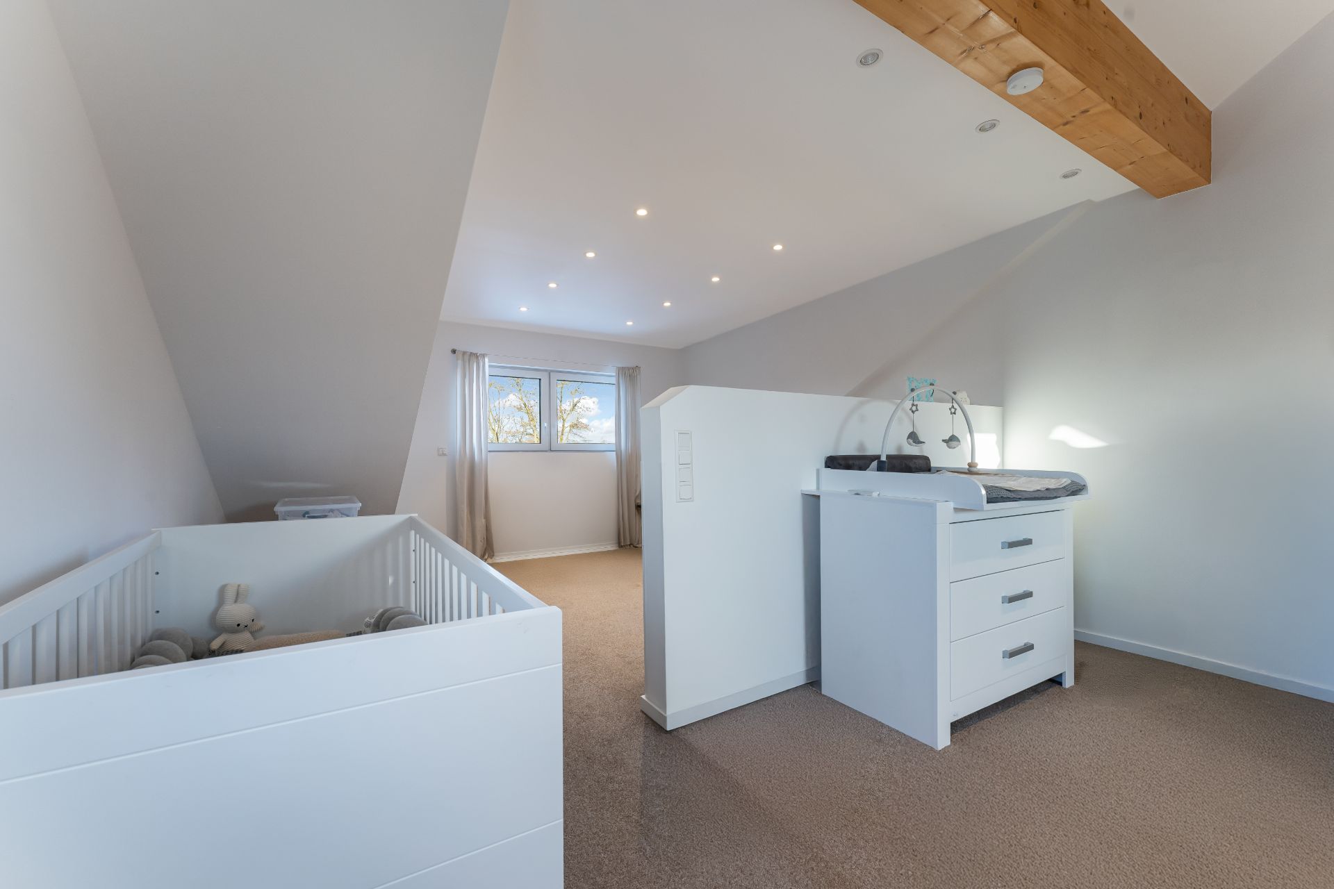 Helles Kinderzimmer mit einem weißen Babybett und einer Wickelkommode unter Dachschrägen.