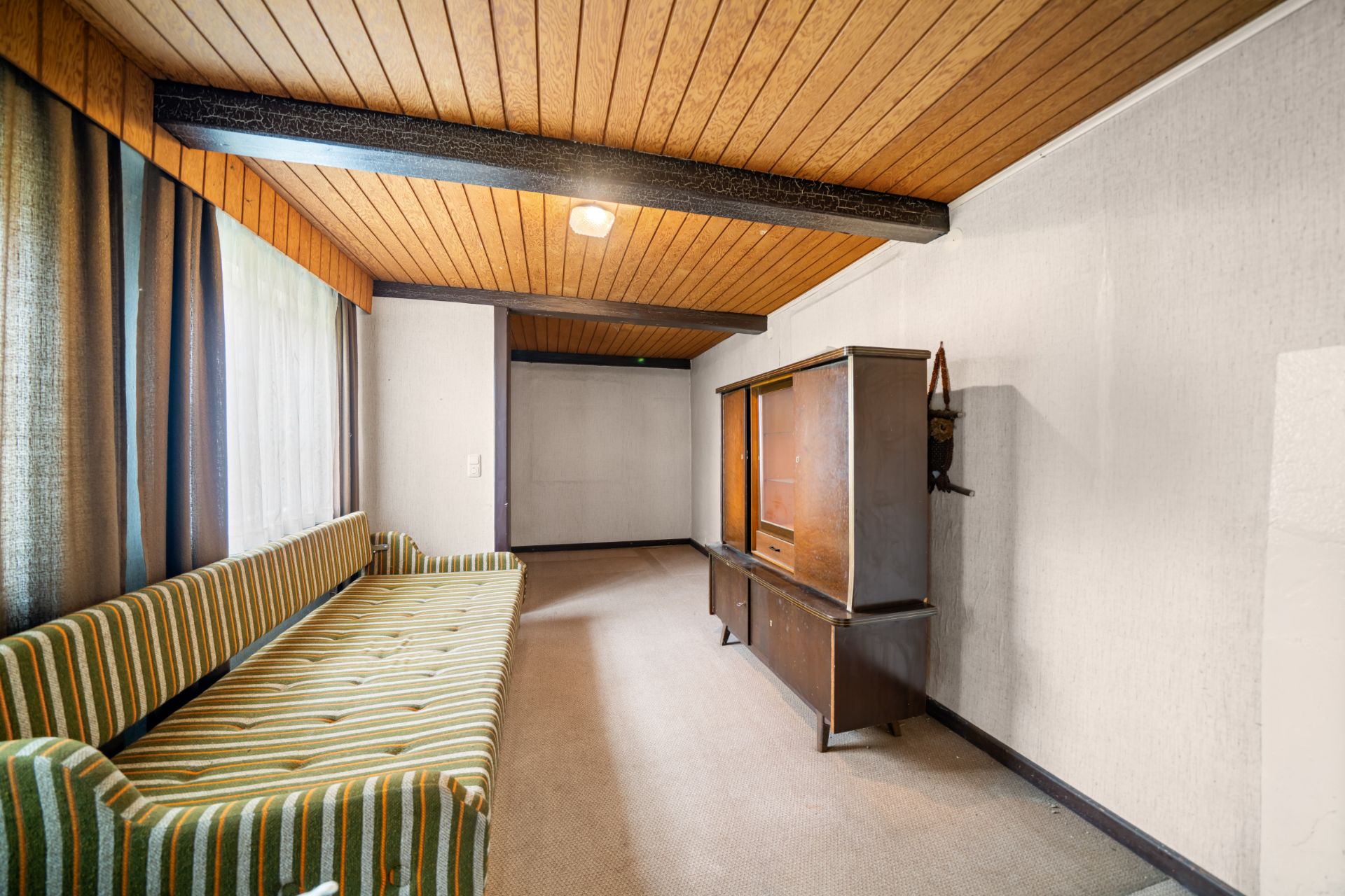 Wohnzimmer mit gestreiftem Sofa, großem Fenster und Holzmöbel an der Wand.