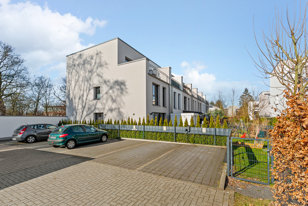 Moderne Reihenhäuser mit Parkplatz und einigen parkenden Autos im Vordergrund.