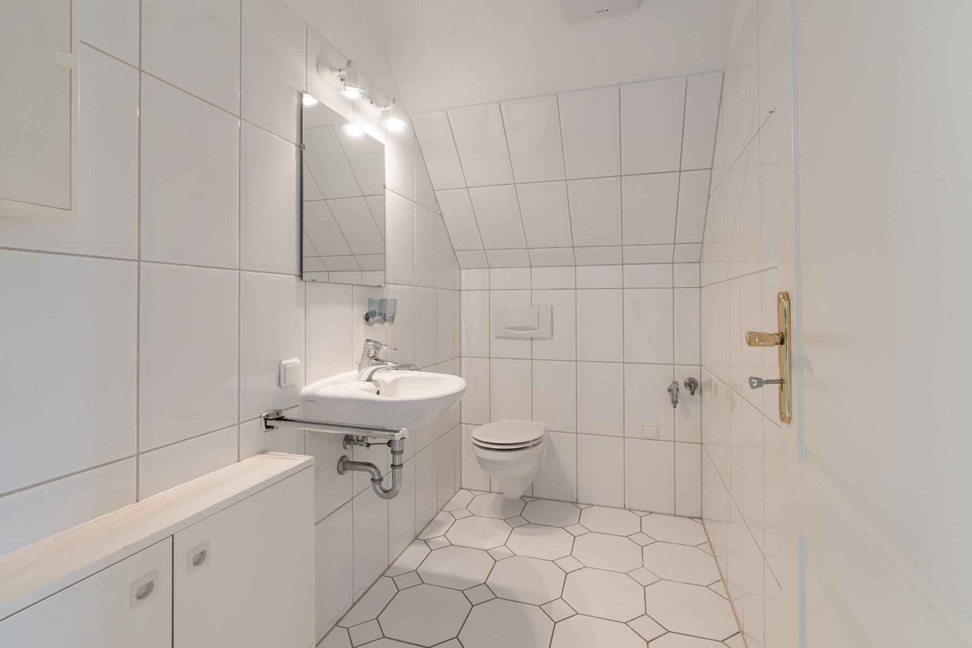 Helles Badezimmer mit Waschbecken, Spiegel und Toilette, weiße Fliesen an Wand und Boden.