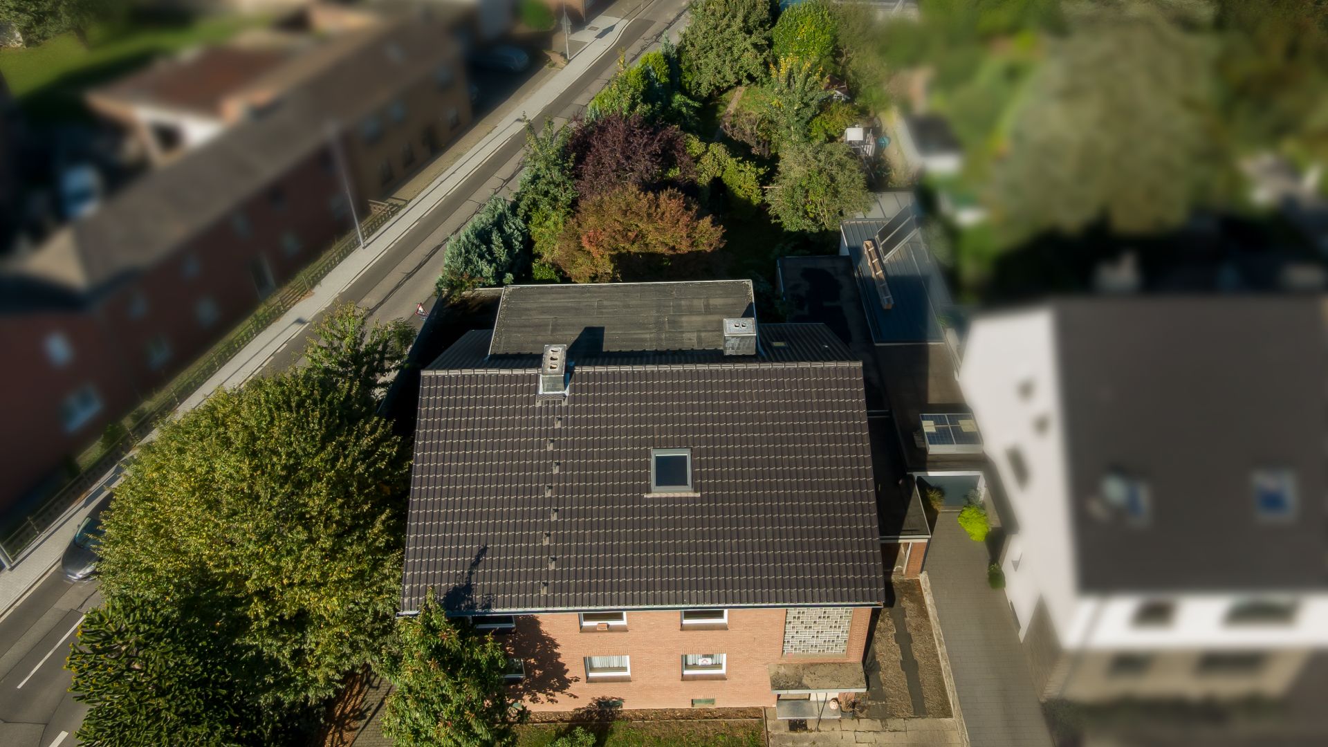 Luftaufnahme eines Wohnhauses mit dunklem Dach, umgeben von Bäumen und Straßen.