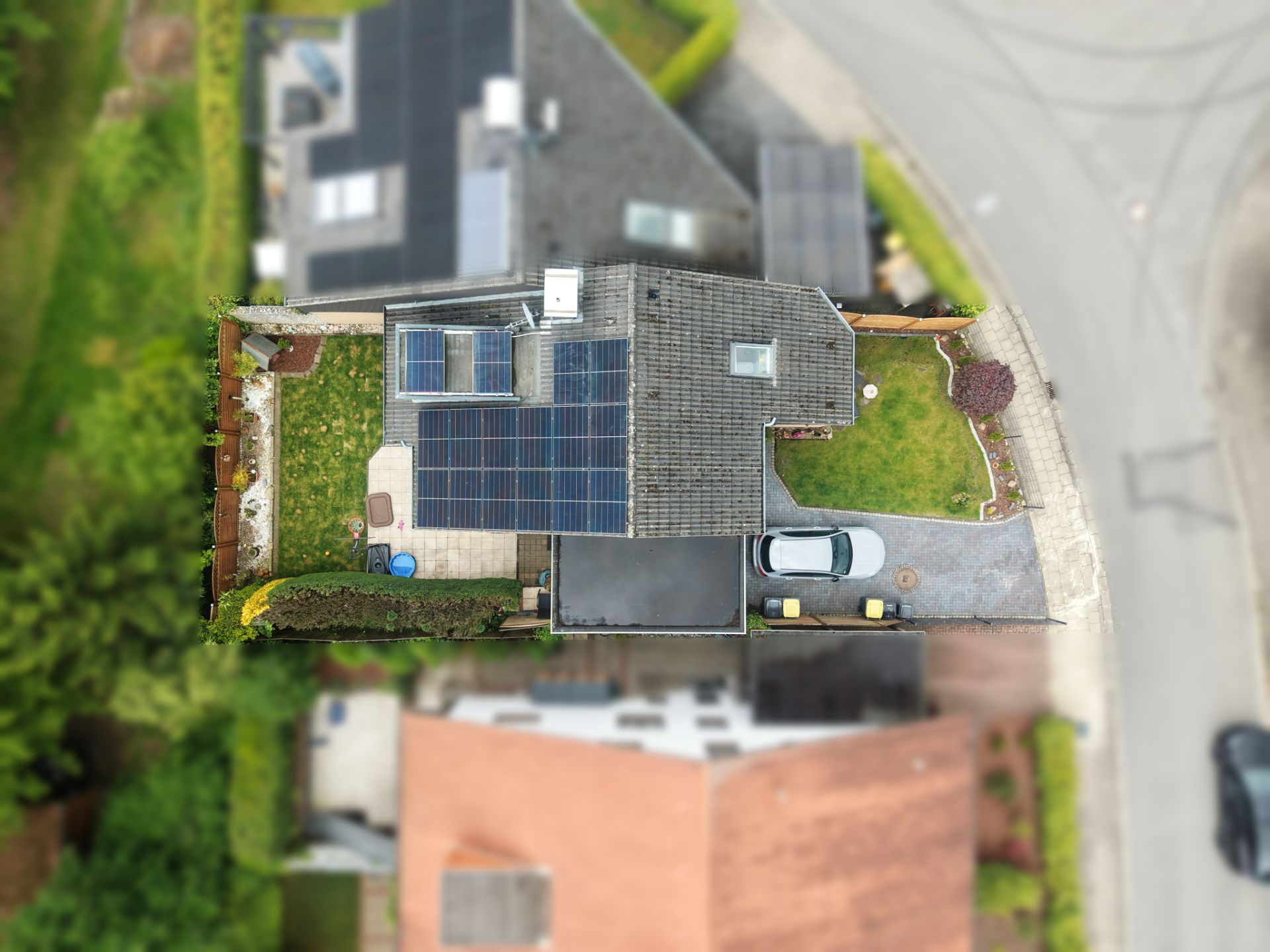 Luftaufnahme eines Einfamilienhauses mit Solarpanels, Garten und geparktem Auto in der Einfahrt.