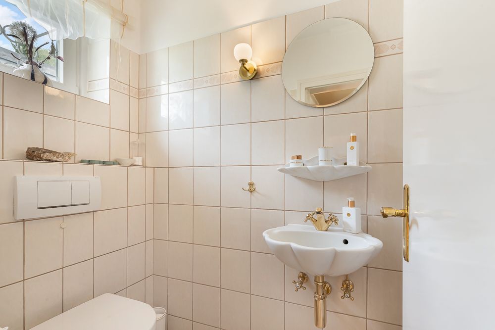 Kleines Badezimmer mit Waschbecken, Spiegel, Toilette und Wandregalen auf hell gefliester Wand.