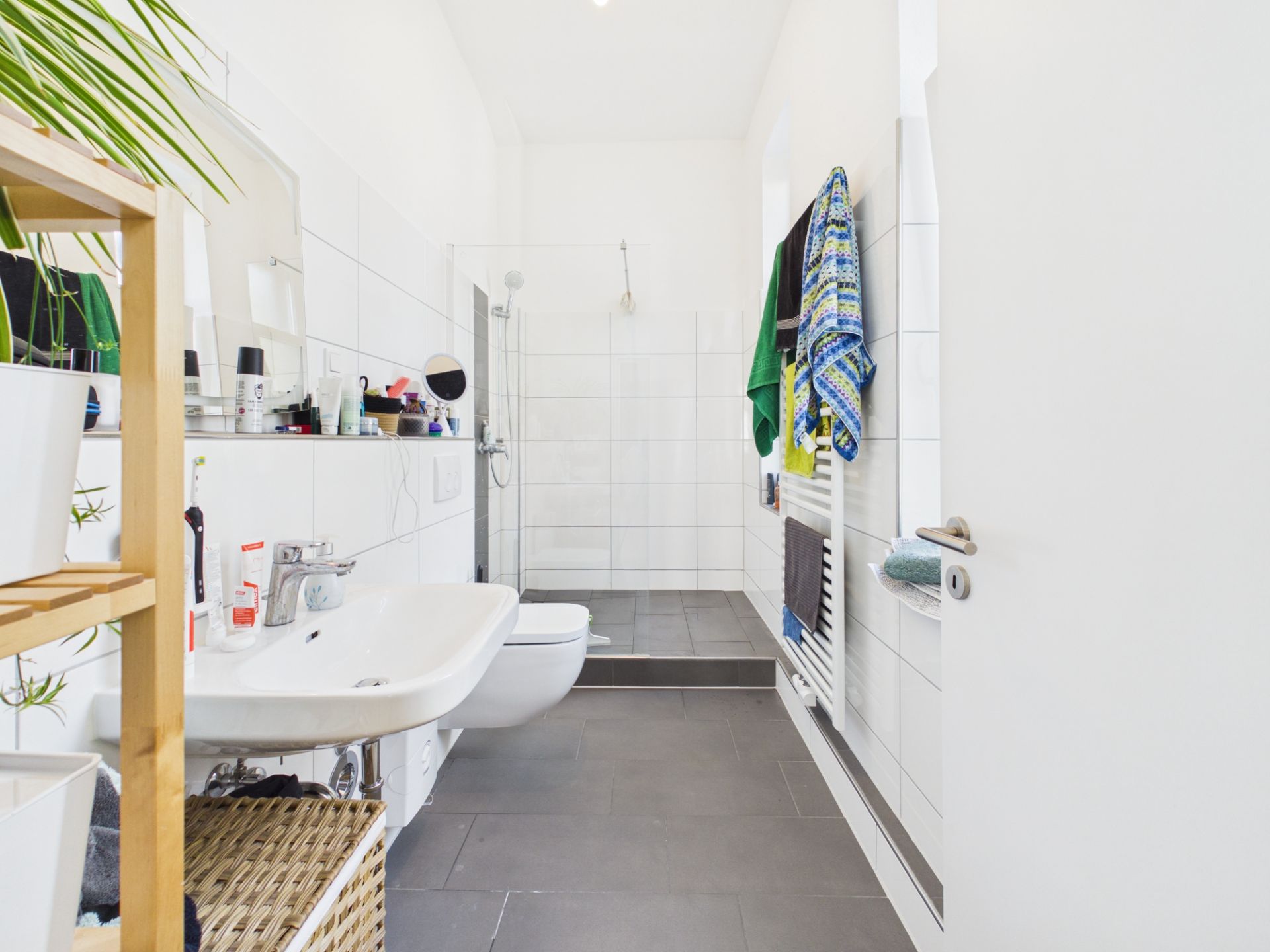 Modernes Badezimmer mit Waschbecken, WC, offener Dusche und Regal mit Pflanzen.