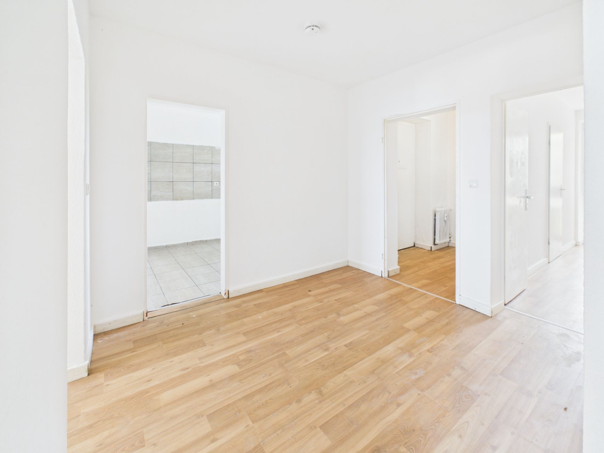 Heller leerer Raum mit Holzfußboden und Türen zu angrenzenden Zimmern.
