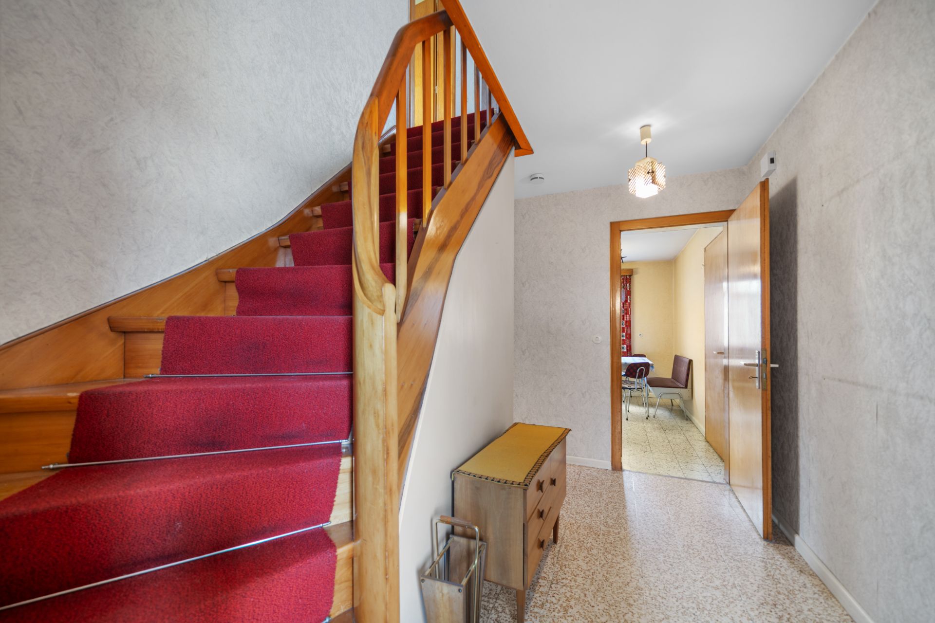 Flur mit Treppe mit rotem Teppich und offener Tür zu einem Esszimmer.