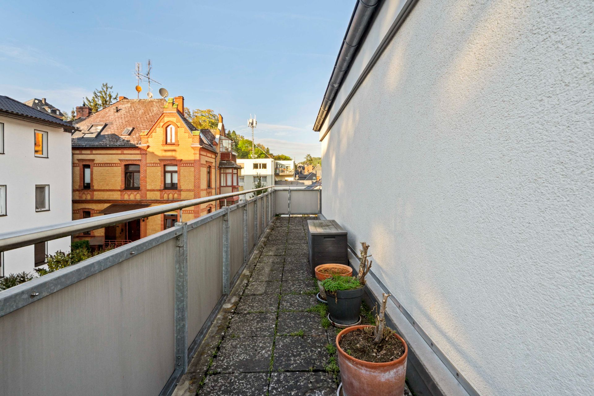 Schmale Dachterrasse mit einigen Blumentöpfen und Ausblick auf Wohnhäuser.
