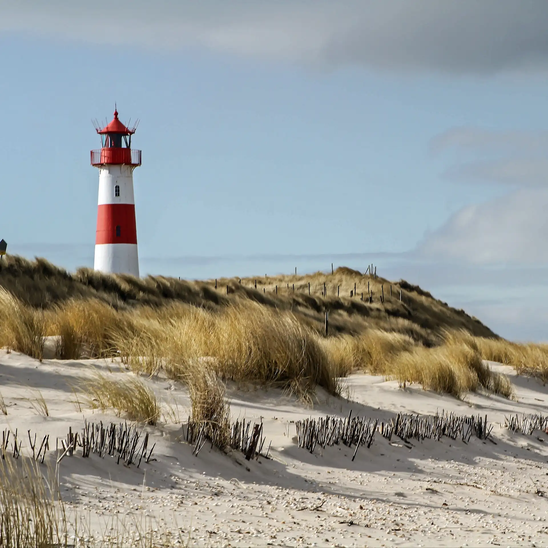 Leuchtturm mit roten und weißen Streifen steht hinter einer Sanddüne mit Gras.