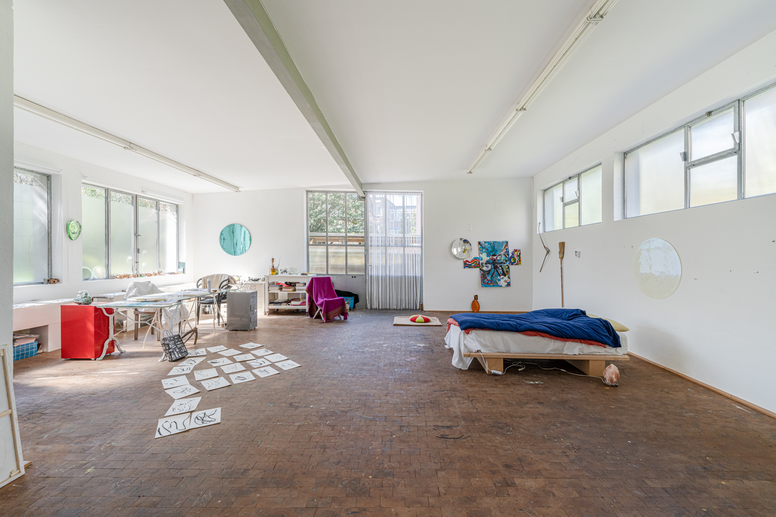 Großer, heller Raum mit Bett, Schreibtisch, Stuhl und Kunstwerken an den Wänden.