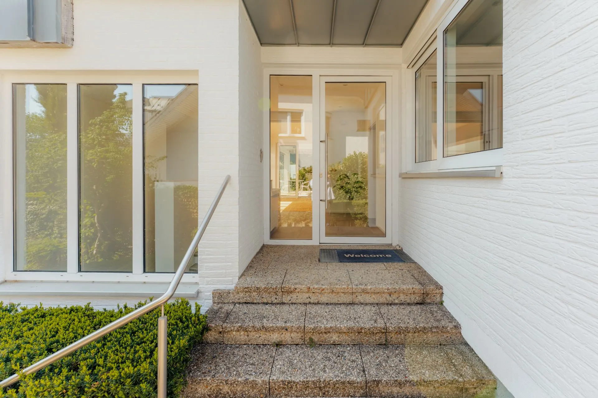 Eingangsbereich eines Wohnhauses mit Glastür, Treppe und Willkommensmatte.