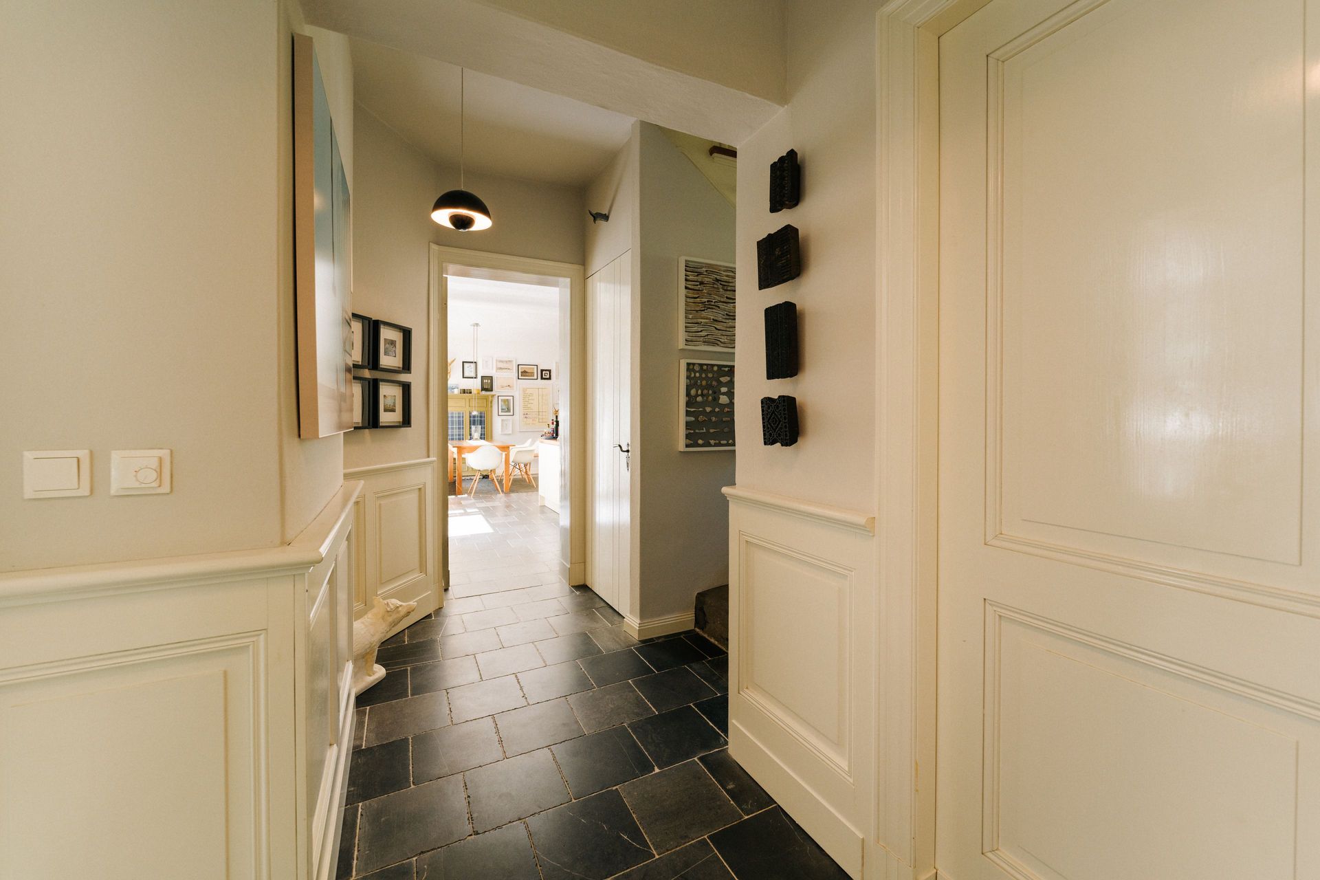 Heller Flur mit dunklem Fliesenboden und Blick in ein Esszimmer mit Wanddekoration.