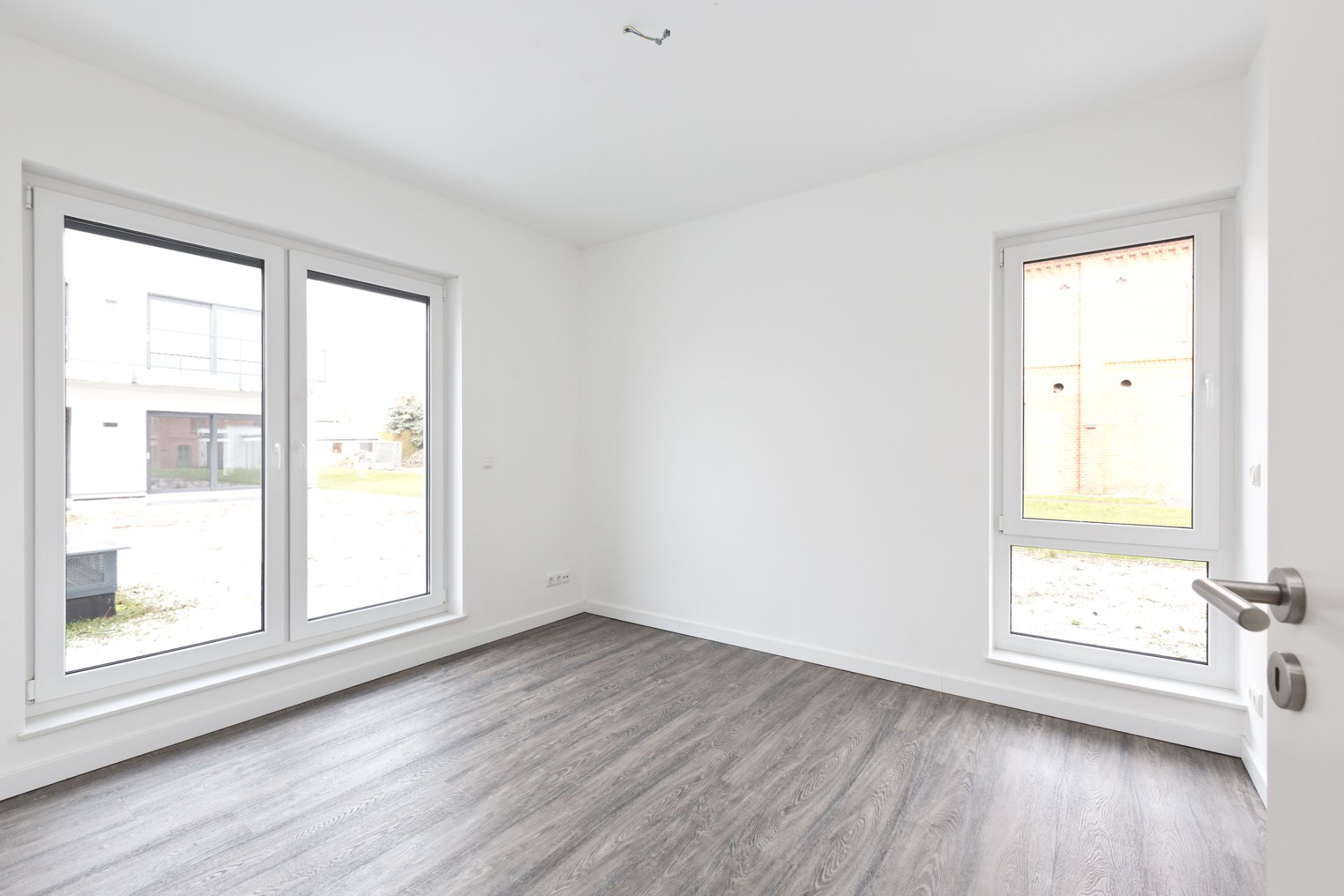 Heller, leerer Raum mit großen Fenstern und dunklem Holzboden.