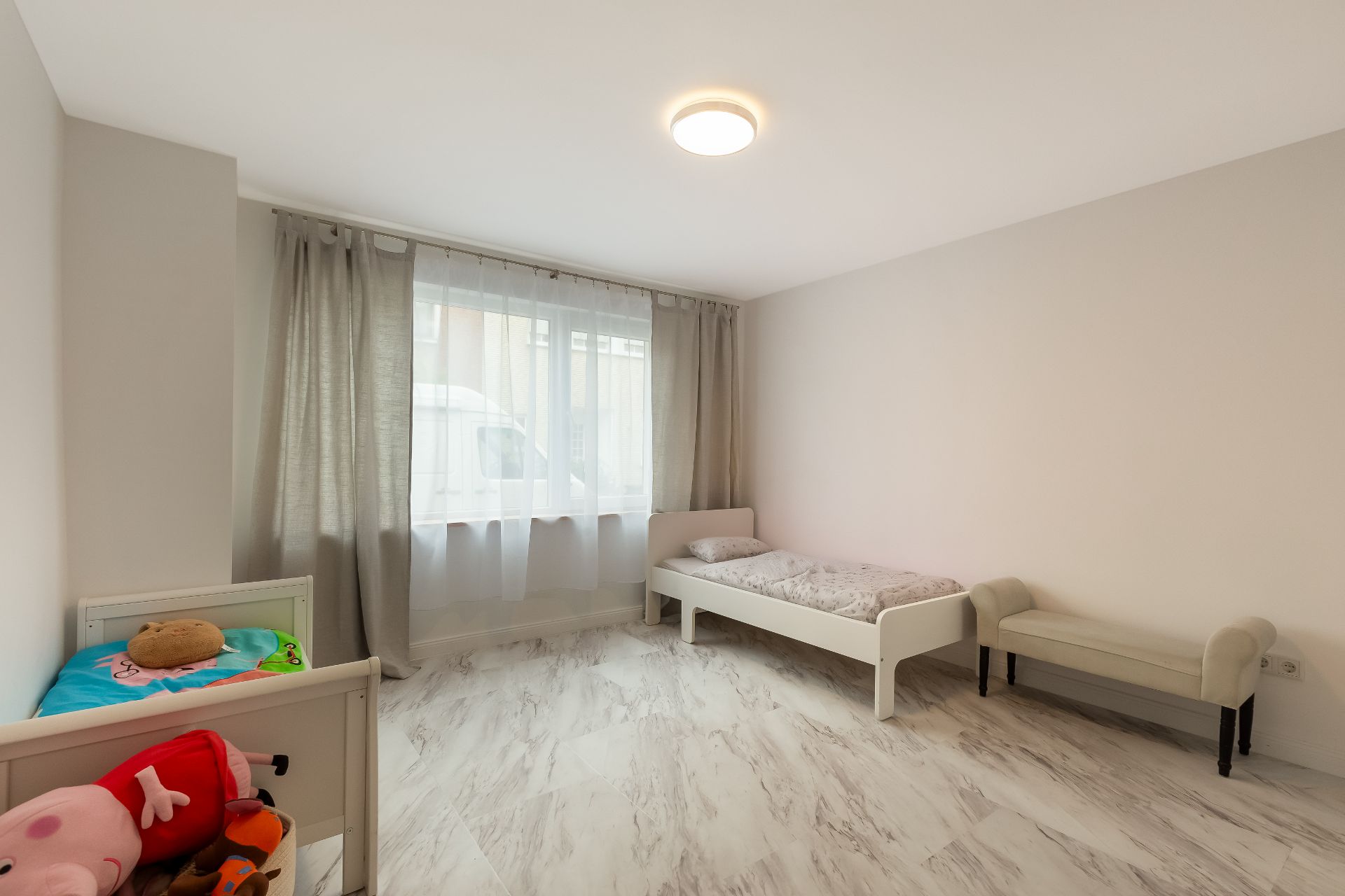Helles Kinderzimmer mit zwei kleinen Betten, Spielzeug und weißem Boden.