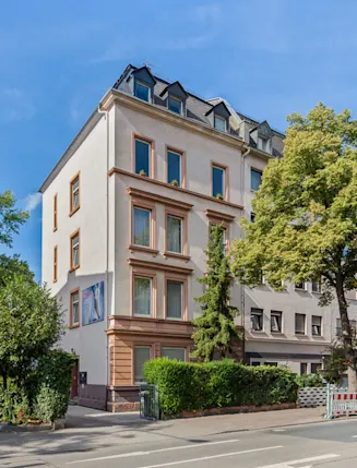 Mehrstöckiges Wohngebäude an einer Straße mit Bäumen und Gehwegen.