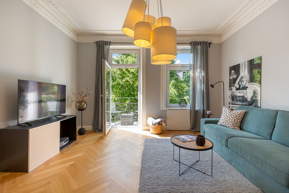 Helles Wohnzimmer mit grünem Sofa, Fernseher, Teppich und Zugang zu einem Balkon.