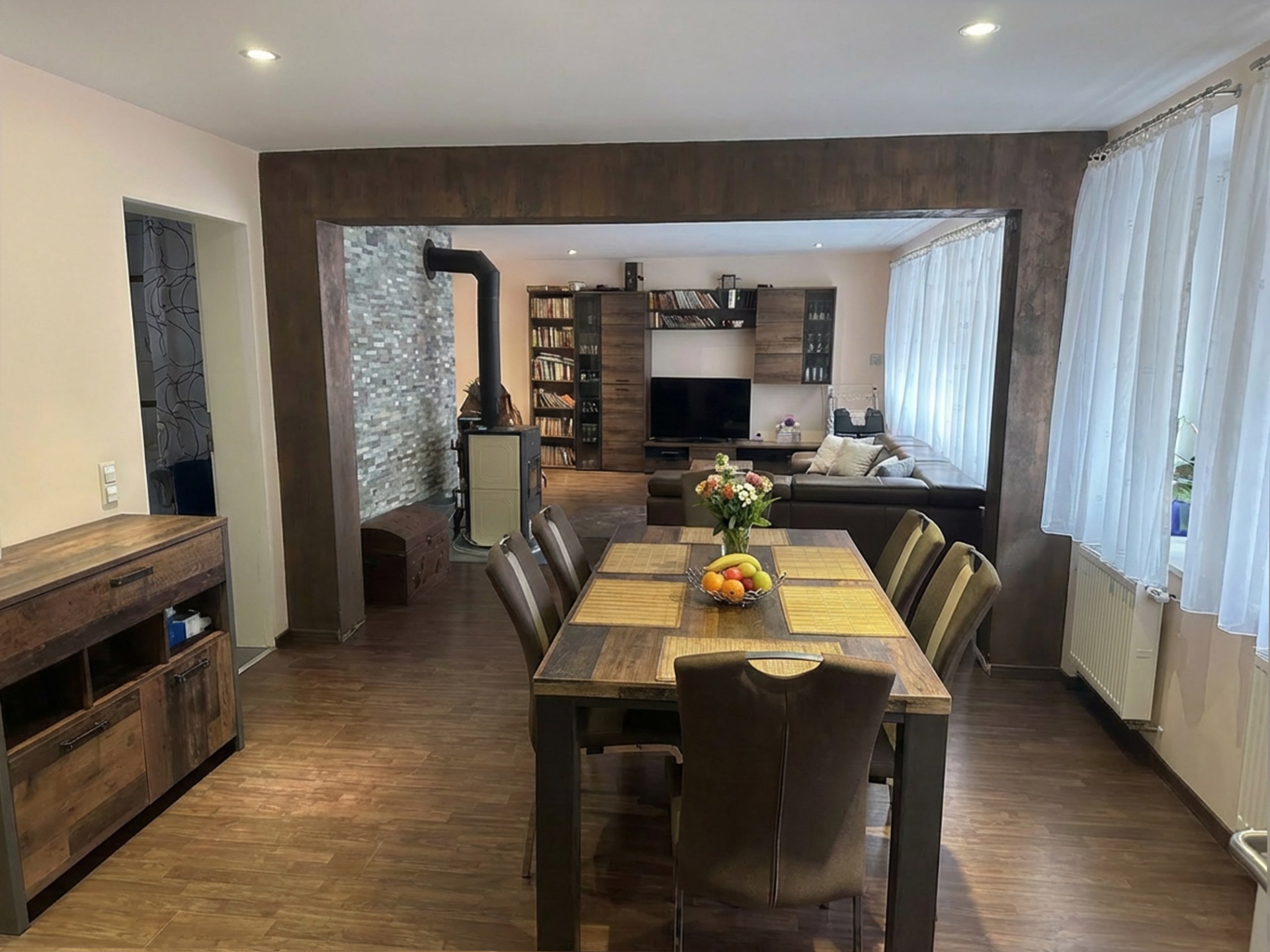 Essbereich mit Holztisch, daneben Wohnzimmer mit Sofa, Regal, Fernseher und Kamin.