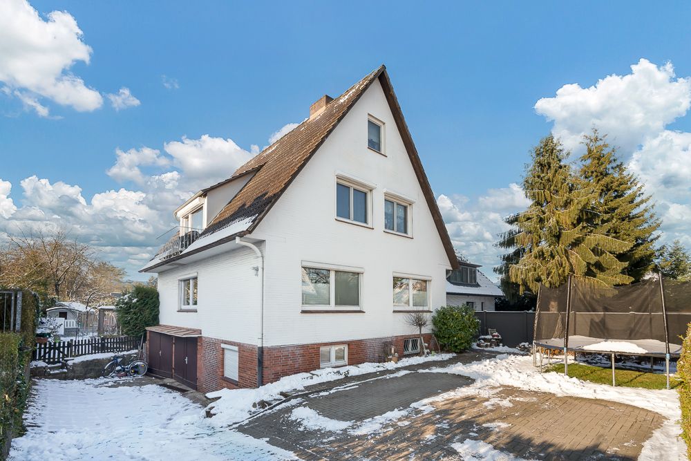 Ein weißes Einfamilienhaus mit Satteldach im Winter, Schnee auf dem Boden, Trampolin im Garten.