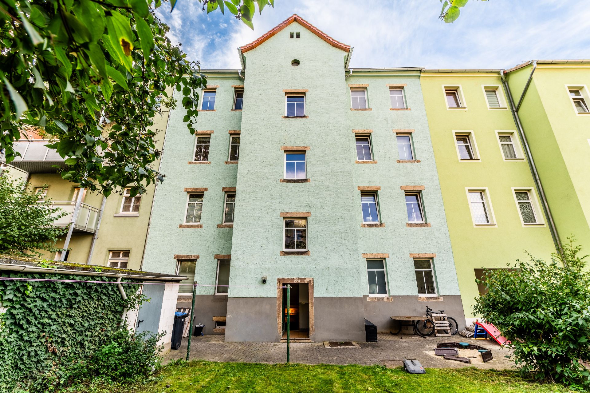 Mehrstöckiges Wohngebäude mit grünem Garten und einigen Gegenständen im Hof.