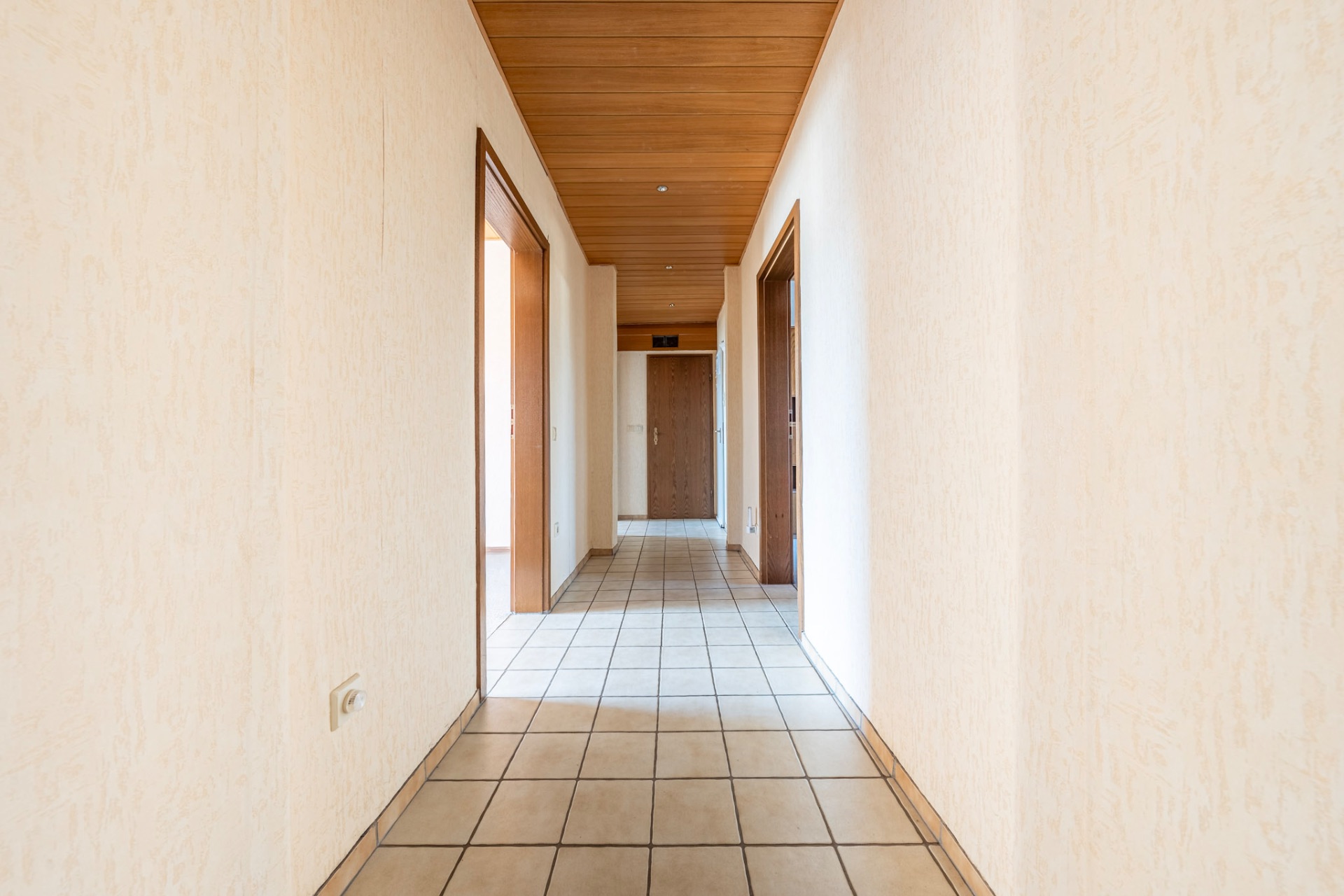 Heller Flur mit gefliestem Boden, Holztüren und Holzdecke in einem Wohnhaus.