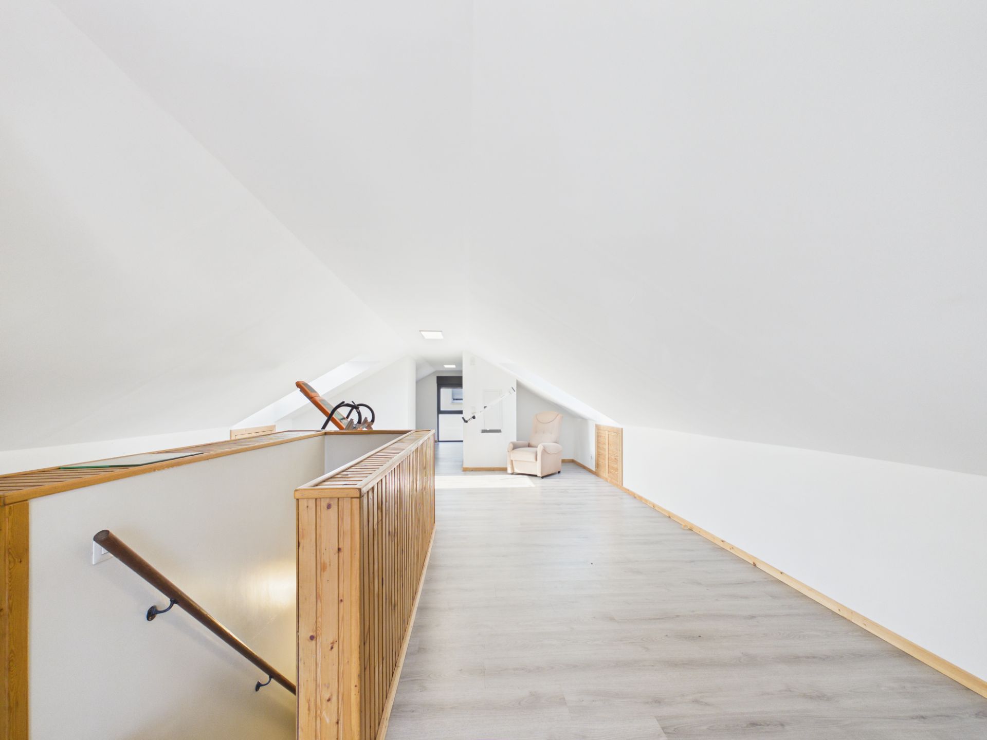 Heller Dachboden mit Holzgeländer, Treppe und Sitzbereich am Ende des Raumes.
