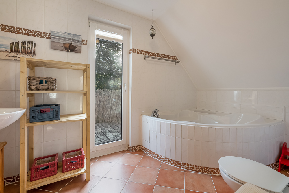 Helles Badezimmer mit Eckbadewanne, Regal, WC und Zugang zur Terrasse.