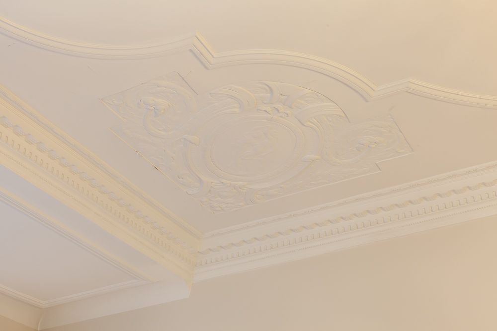 Weiße Stuckdecke mit dekorativem Ornamentmuster in einem Wohnraum.