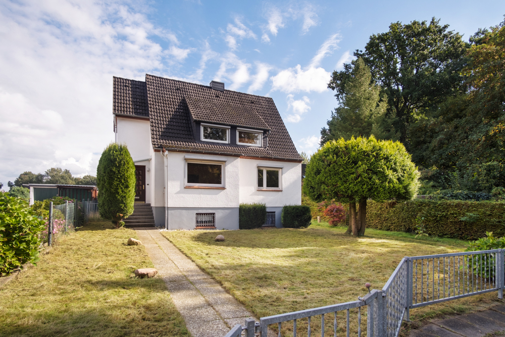 Zweistöckiges Einfamilienhaus mit Satteldach, Garten und zwei Bäumen vorne.