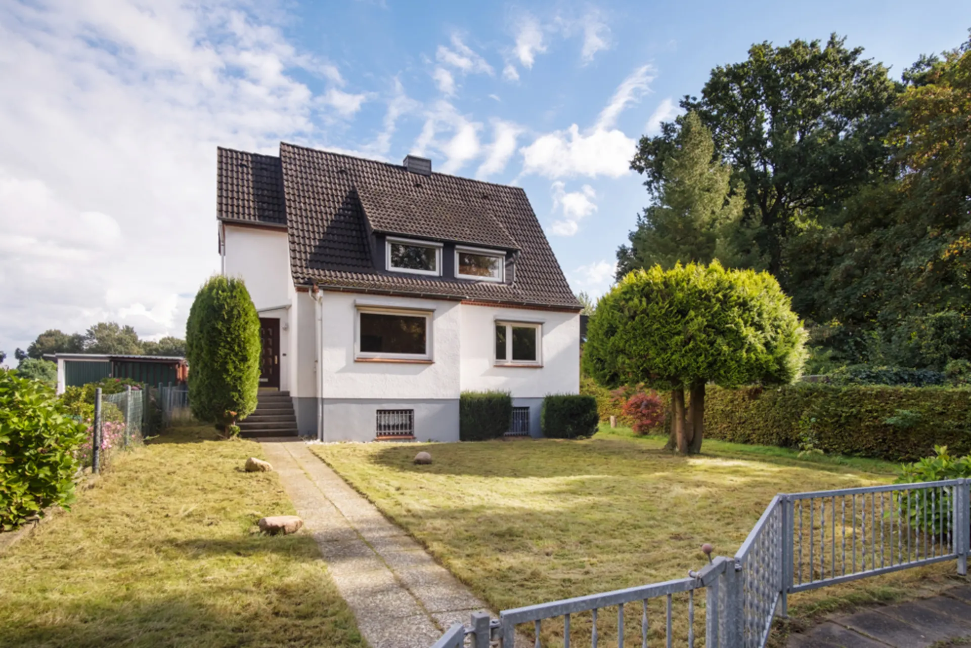 Zweistöckiges Einfamilienhaus mit Satteldach, Garten und zwei Bäumen vorne.