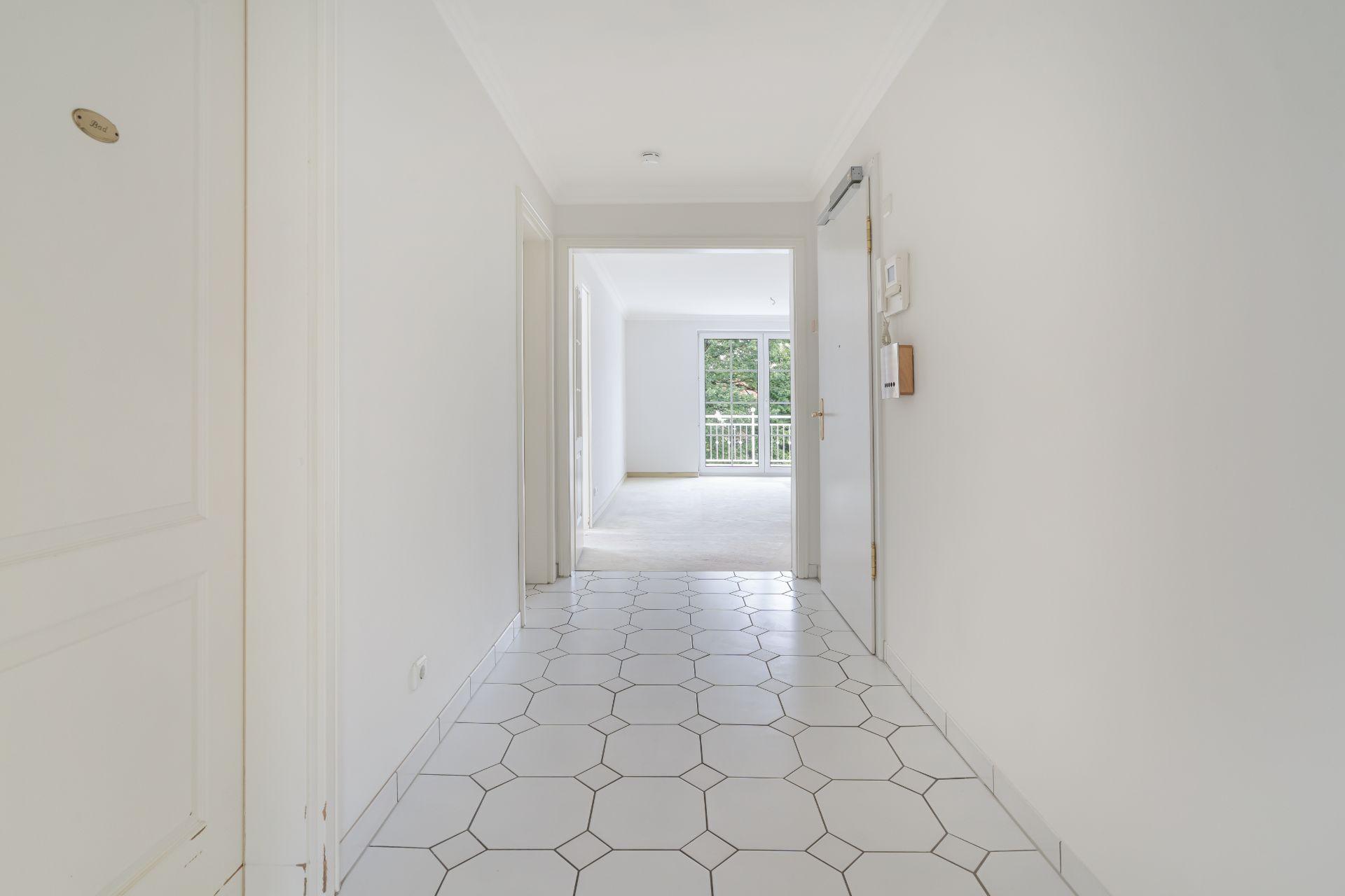 Heller Flur mit weißen Wänden und sechseckigen Bodenfliesen, Blick auf Wohnzimmer mit Balkon.