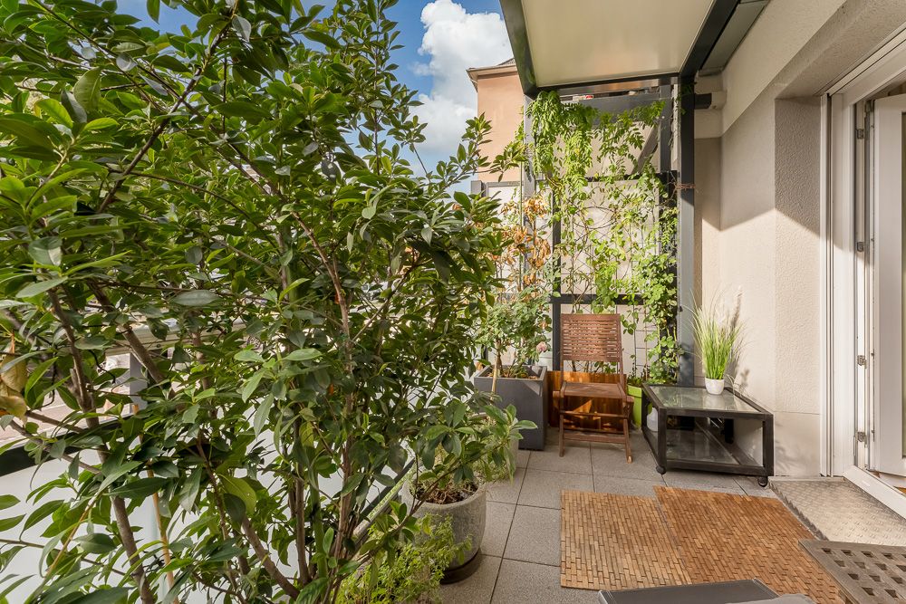 Balkon mit vielen Pflanzen, einem Holzstuhl und einem kleinen Glastisch.