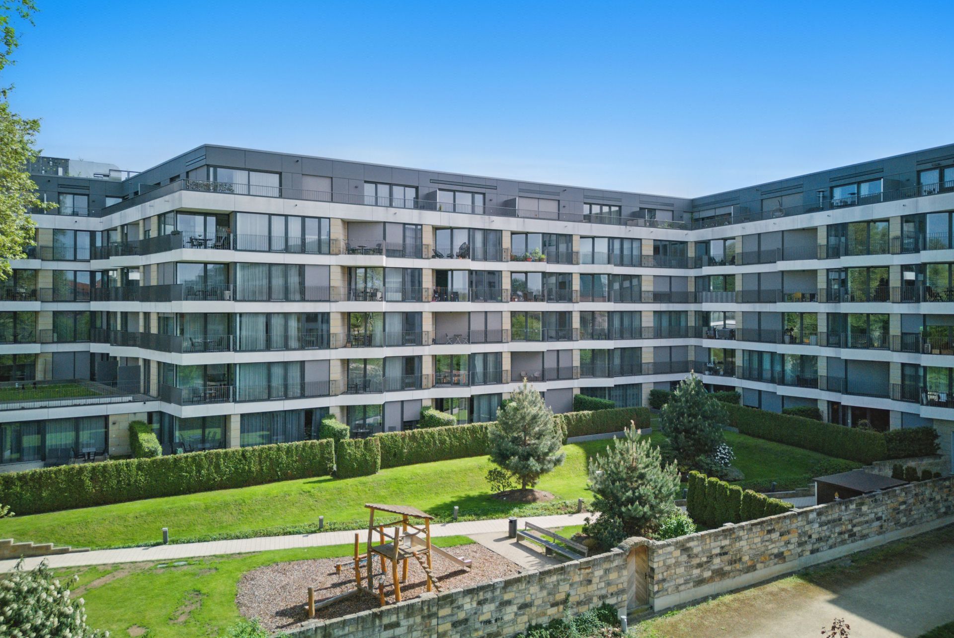 Modernes Wohnhaus mit mehreren Stockwerken und einem begrünten Innenhof mit Spielplatz.