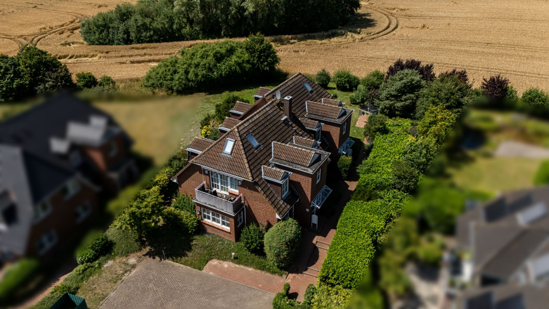 Luftaufnahme eines großen Backsteinhauses mit Garten, umgeben von Feldern und Bäumen.