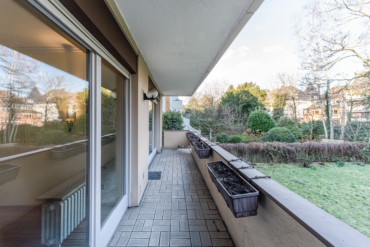 Langer Balkon mit Pflanzkästen, Blick auf Garten und Bäume.