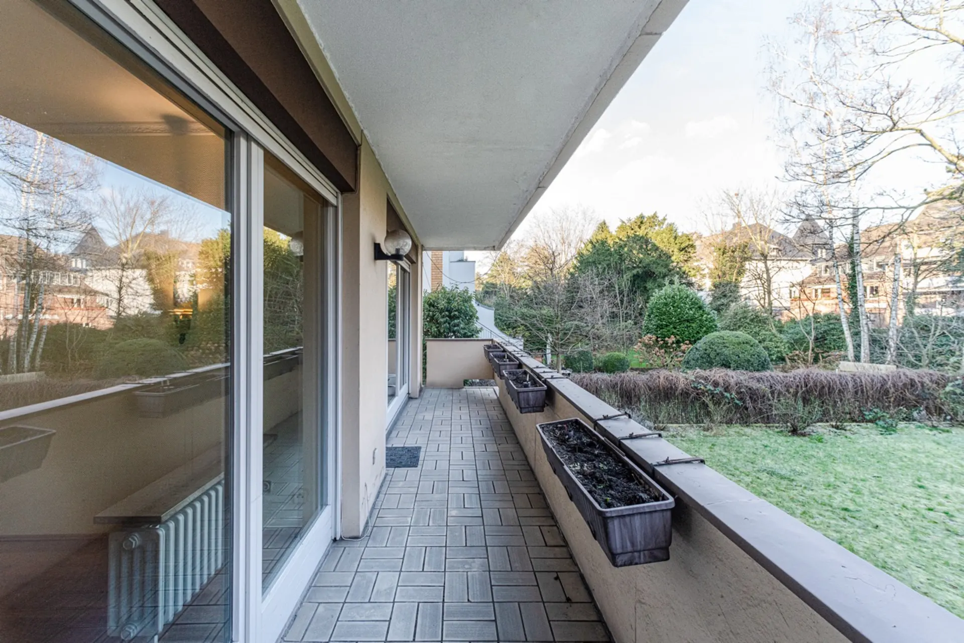 Langer Balkon mit Pflanzkästen, Blick auf Garten und Bäume.