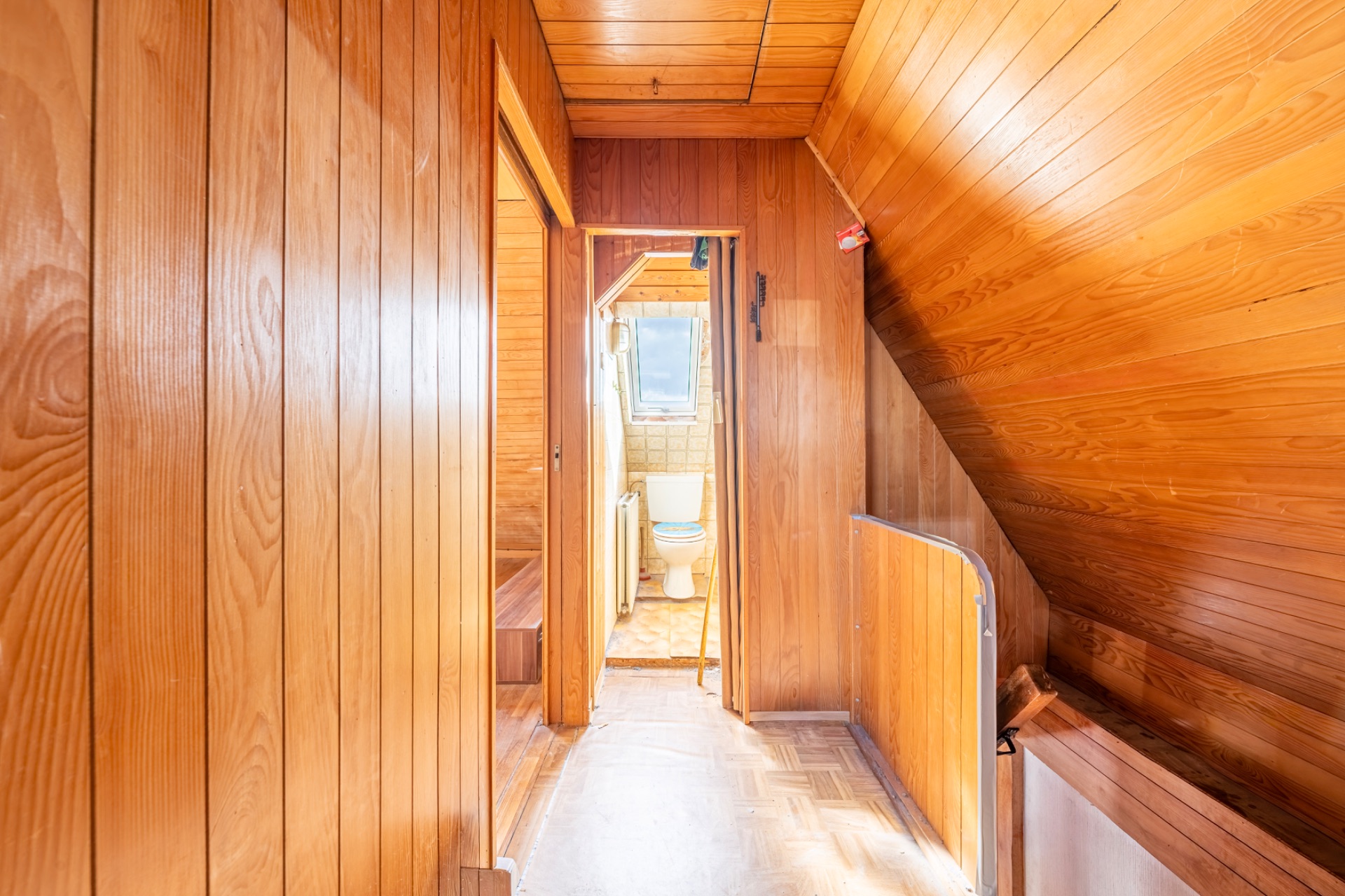 Flur mit Holzvertäfelung, Blick auf ein Badezimmer mit Toilette und Fenster.