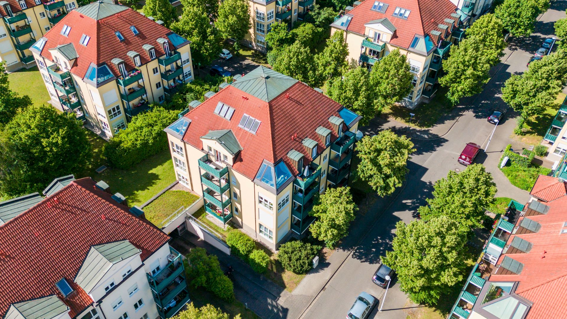 Luftaufnahme von Wohngebäuden mit roten Dächern und grünen Bäumen entlang der Straßen.