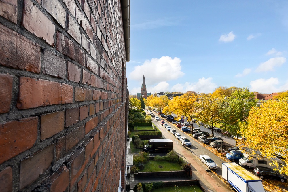 Blick von einem Backsteingebäude auf eine Straße mit vielen Autos und gelben Bäumen.