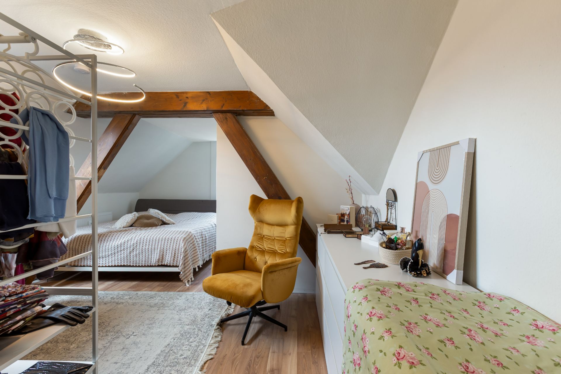 Dachzimmer mit gelbem Sessel, Bett, Kleiderständer und Kommode mit Spiegel.