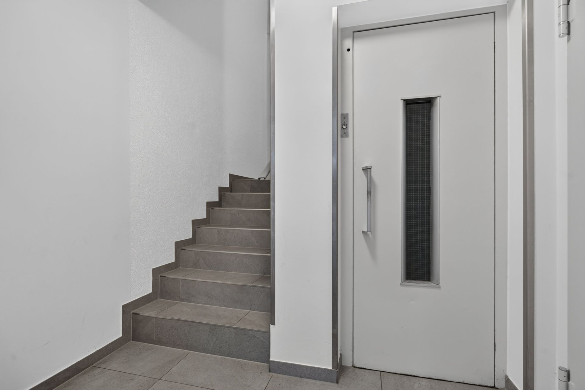 Treppe und Aufzug in einem hellen Flur eines Wohngebäudes.