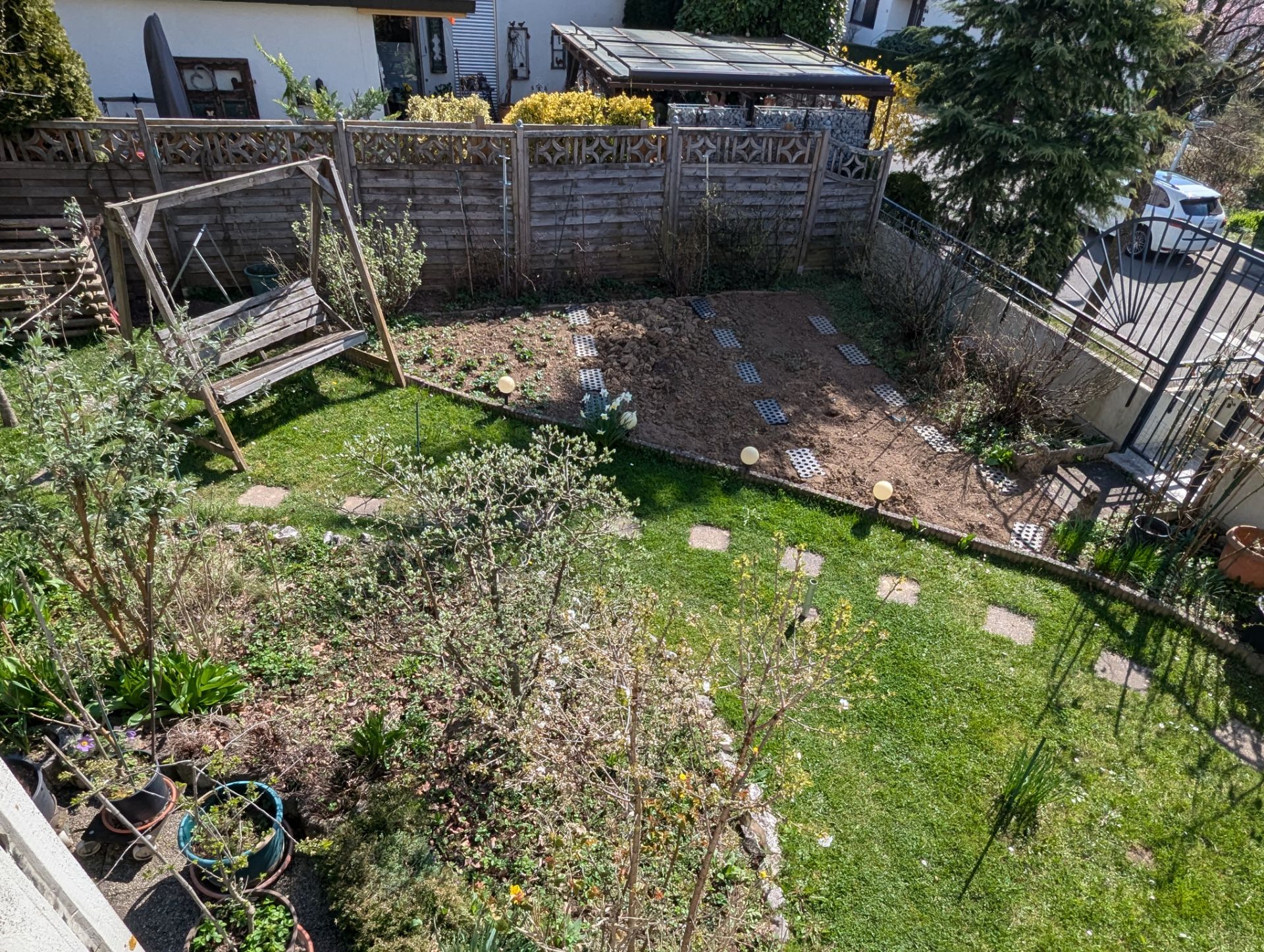 Garten mit Holzschaukel, Rasen, Beeten und Steinplatten, umgeben von einem Holzzaun.