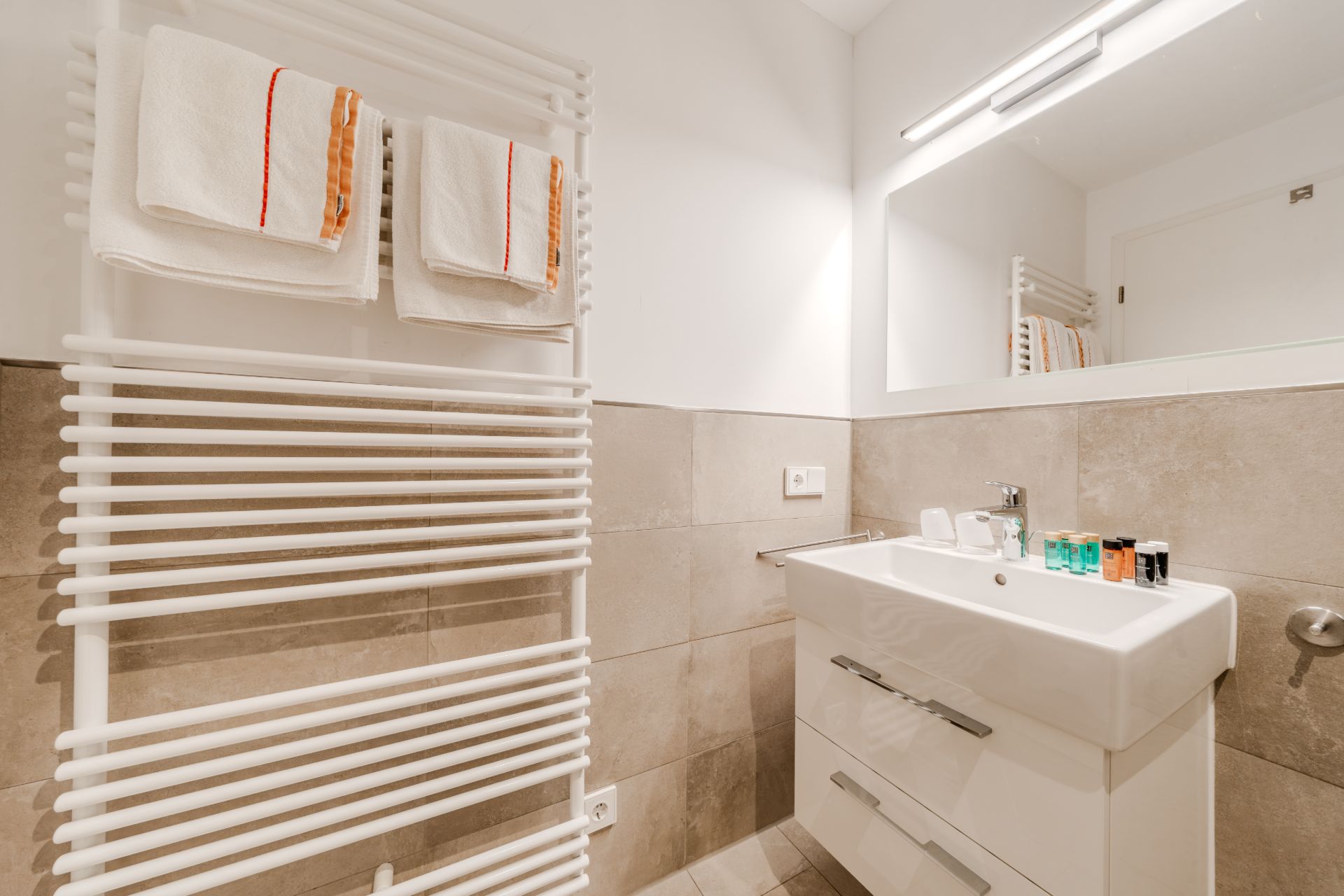 Modernes Badezimmer mit Handtuchheizkörper, Waschbecken und großem Spiegel.