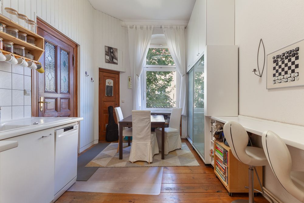Heller Raum mit Esstisch, Stühlen, Fenster, Küchenzeile und Regal mit Büchern.