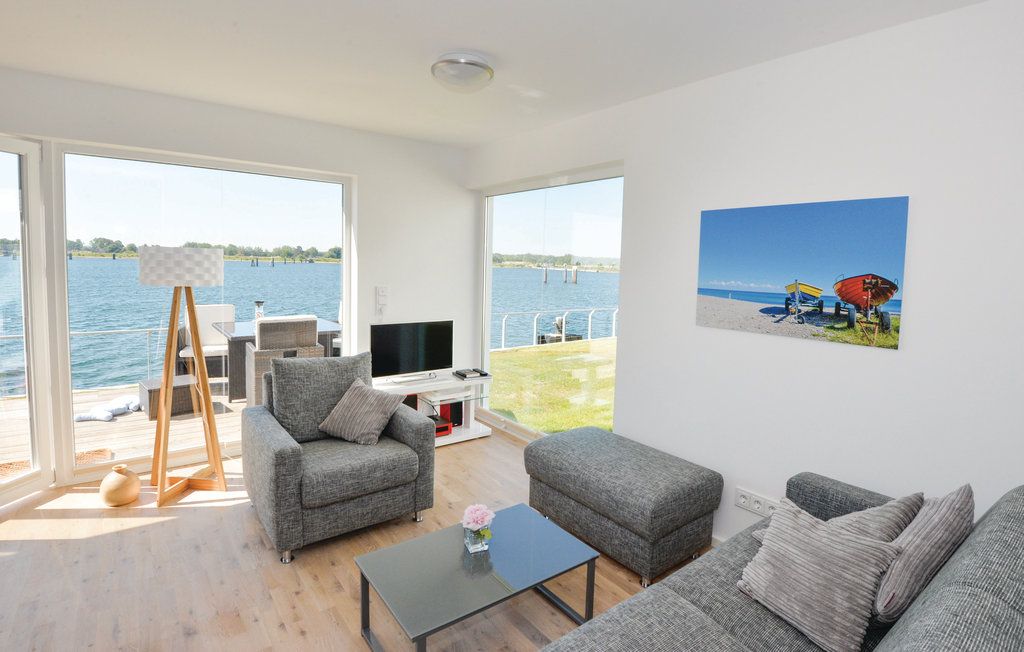 Helles Wohnzimmer mit grauen Sofas, Couchtisch, Stehlampe und großem Fenster mit Seeblick.