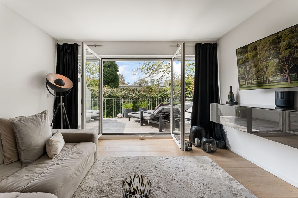 Modernes Wohnzimmer mit Sofa, Teppich und Zugang zu einer Terrasse mit Liegestühlen.