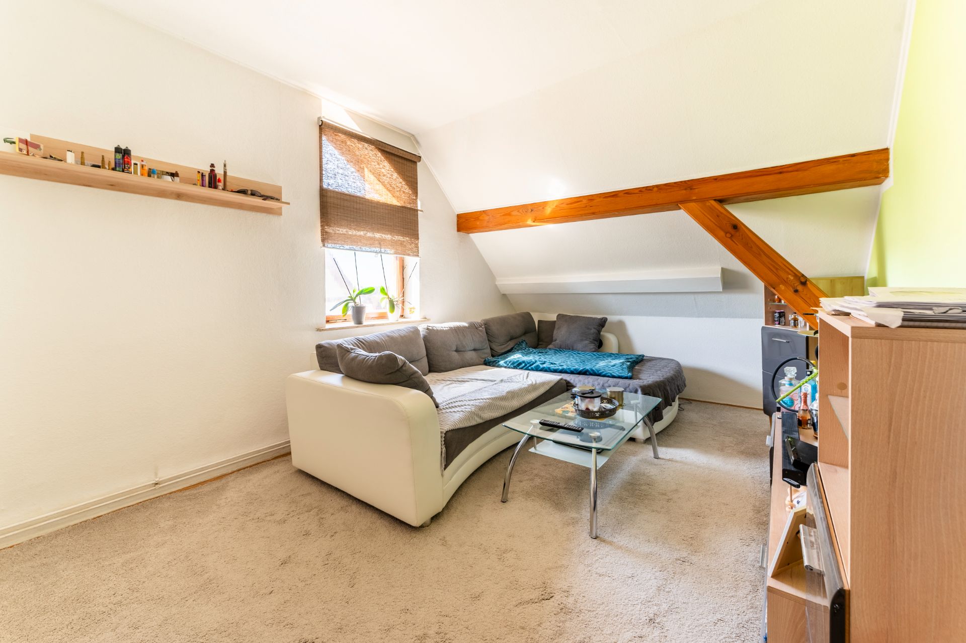 Helles Wohnzimmer mit Ecksofa, Glastisch und Regal unter einer Dachschräge.